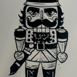 May include: Black and white illustration of a toy soldier nutcracker with a large moustache and a tall hat. The nutcracker is holding a sword in its right hand.