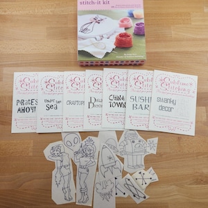 May include: A stitch-it kit with a box showing a cat embroidery design, thread spools, and instructions. Includes multiple embroidery patterns with phrases like "Pirates Ahoy!" and "Sushi Bar", plus various outline designs.