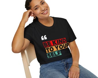 以下が含まれることがあります： 白、赤、オレンジ、緑で「BE KIND TO YOURSELF」と書かれた黒いTシャツ。白い引用符のグラフィックが付いています。モデルはブルージーンズを着用し、木製の椅子に座っています。