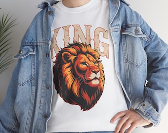 May include: White t-shirt featuring a detailed illustration of a lion's head with a fiery orange and red mane. The word "KING" is printed above the lion in a vintage-style font. The shirt is worn with a blue denim jacket.