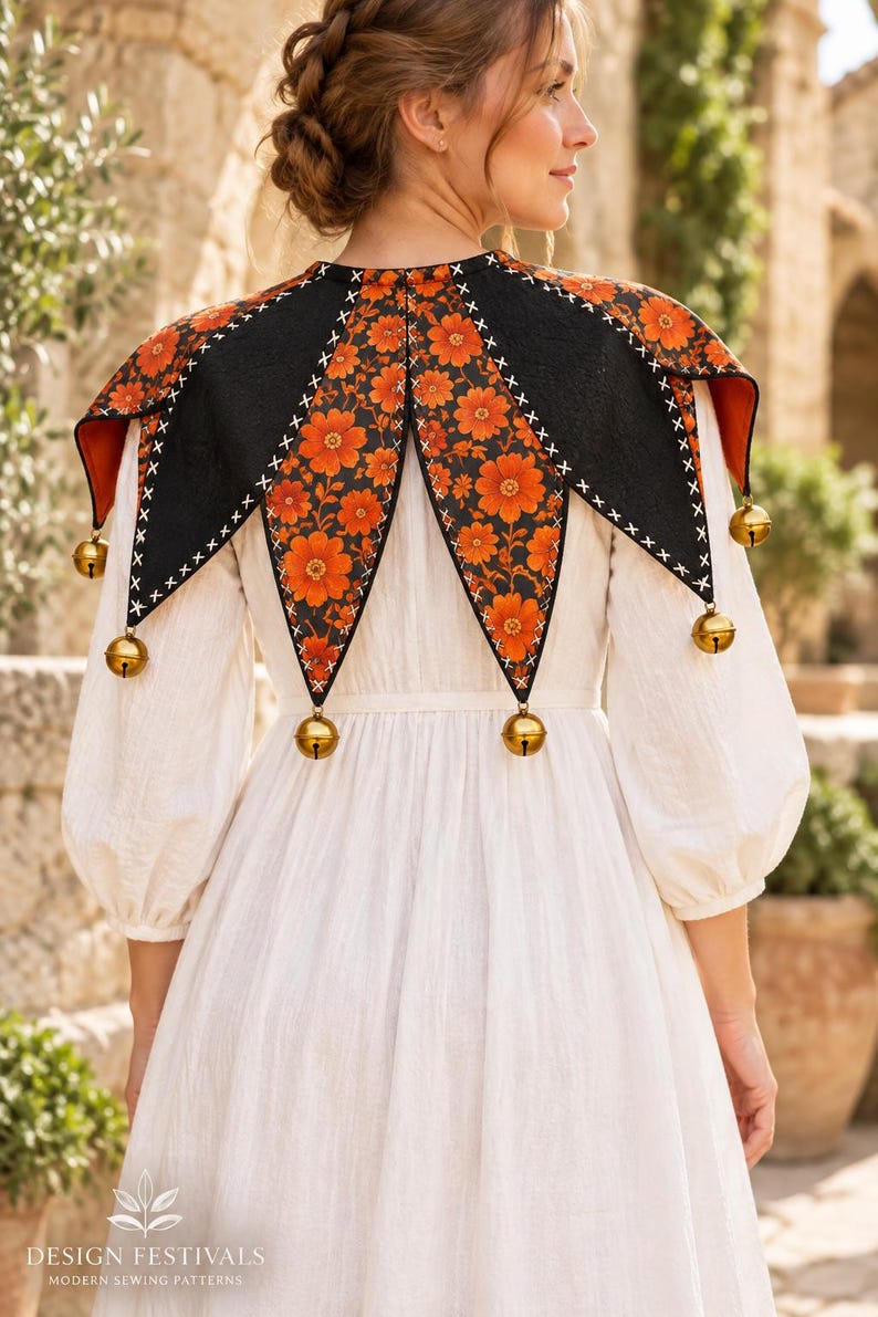 May include: A white long-sleeved dress paired with a black and orange floral print jester-style collar. The collar features pointed panels, white cross-stitch detailing along the edges, and gold-toned metal bells attached to each of the six points.