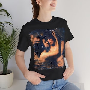 Könnte beinhalten: Schwarzes T-Shirt mit einem romantischen Gemälde eines sich umarmenden und küssenden Paares. Das Kunstwerk hat einen himmlischen Hintergrund mit Blau-, Gold- und Weißtönen. Das Design ist auf ein kurzärmeliges T-Shirt mit Rundhalsausschnitt gedruckt.