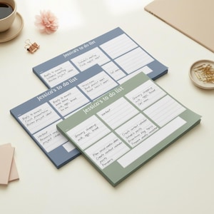 May include: Three notepads with the text "Jessica's to do list" in a light blue and green color scheme. Each notepad has sections for tasks, with handwritten notes. A cup of coffee, a flower, and paper clips are in the background.