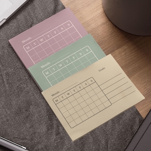May include: Three pastel-colored sticky note pads with a monthly calendar grid and the word "Month" printed at the top. The bottom pad also includes the word "Goals". The pads are in shades of mauve, mint green, and beige.