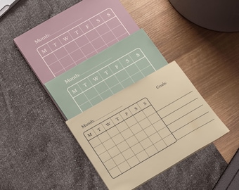 May include: Three pastel-colored sticky note pads with a monthly calendar grid and the word "Month" printed at the top. The bottom pad also includes the word "Goals". The pads are in shades of mauve, mint green, and beige.