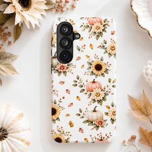 May include: A white smartphone case featuring a repeating pattern of orange and white pumpkins, yellow sunflowers, and scattered autumn leaves. The case has a vertical camera cutout on the upper left side with three circular lenses visible.
