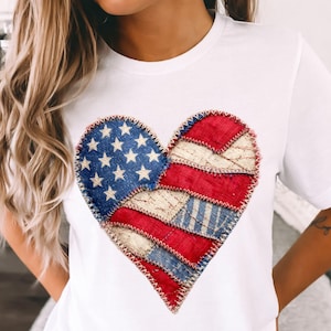 May include: White t-shirt featuring a heart-shaped design. The heart is composed of patches in red, white, and blue, resembling the American flag. The design includes stars and stripes, with a stitched border.