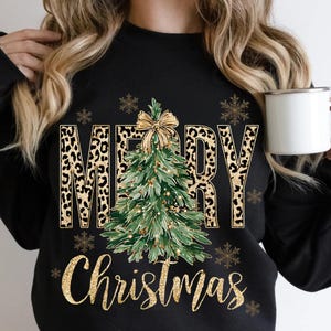 K&ouml;nnte beinhalten: Schwarzes Sweatshirt mit einem festlichen Design. Die Worte "MERRY CHRISTMAS" sind in goldenem Glitzer und Leopardenmuster dargestellt. Ein gr&uuml;ner Weihnachtsbaum mit goldener Schleife befindet sich in der Mitte.