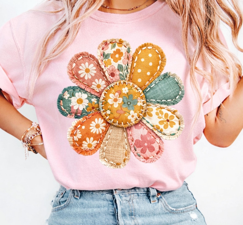 Może przedstawiać: Jasnor&oacute;żowa koszulka z dużym, kolorowym wzorem kwiatowym. Kwiat ma płatki z tkaniny w r&oacute;żnych wzorach i kolorach, w tym nadruki kwiatowe i kropki. Projekt jest wyśrodkowany na koszulce.