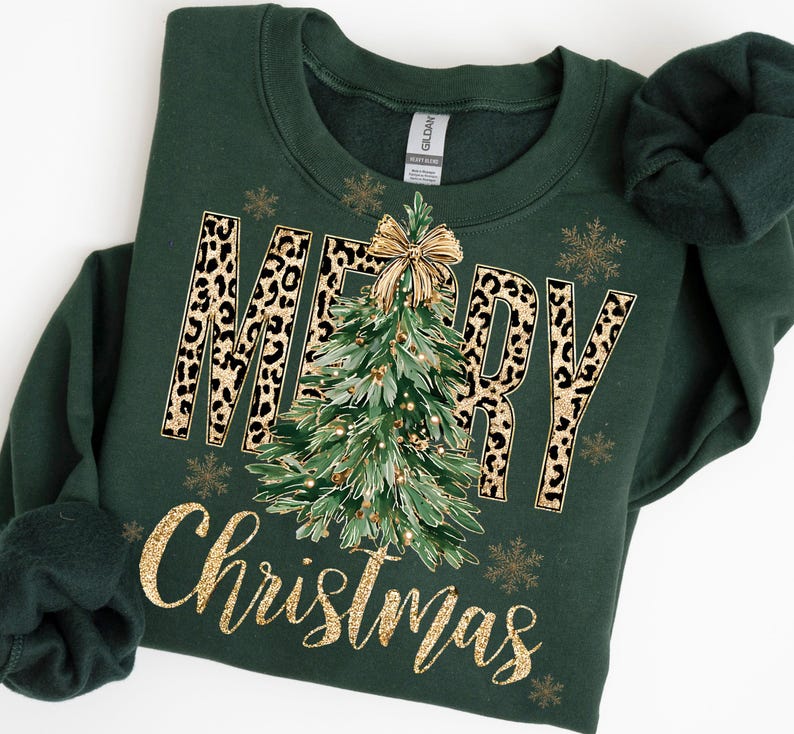 K&ouml;nnte beinhalten: Ein dunkelgr&uuml;nes Sweatshirt mit den Worten "MERRY Christmas" in Goldglitzer und Leopardenmuster. Ein Weihnachtsbaum mit einer goldenen Schleife befindet sich in der Mitte. Goldene Schneeflocken sind um den Text herum verstreut.