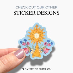 May include: A sticker design featuring a gold monstrance with a white center, surrounded by floral accents in pink, red, and blue, set against a light blue background. The sticker has the text "CHECK OUT OUR OTHER STICKER DESIGNS" and "PROVIDENCE PRINT CO."