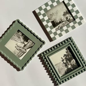 Puede incluir: Tres marcos de fotos decorativos en tonos verdes y blancos. Uno tiene un borde festoneado, otro un patrón de tablero de ajedrez y el tercero un borde punteado. Cada marco contiene una fotografía en blanco y negro.