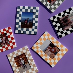 Puede incluir: Una colección de marcos de fotos a cuadros en varios colores, incluyendo rojo, negro, gris, beige y naranja. Cada marco contiene una fotografía diferente. Los marcos están dispuestos sobre una superficie púrpura.