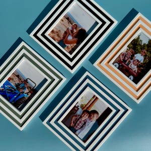May include: Four diamond-shaped picture frames with family photos. The frames are white, black, and various shades of blue and tan. The photos show people, including children, in outdoor settings. The frames are arranged on a light blue surface.