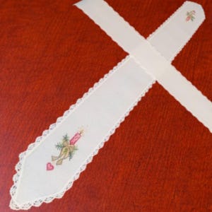 May include: Two white, embroidered Christmas table runners with scalloped edges. One runner features a candle, greenery, and a heart. The other has a floral design. The runners are on a red surface.