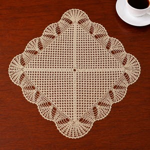 May include: A beige, square doily with a detailed, openwork design. The doily features a scalloped edge with fan-like patterns. The intricate crochet work is displayed on a dark brown wooden surface, with a white teacup and saucer in the background.