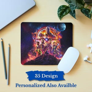 May include: A rectangular mousepad featuring a colorful graphic of various characters from a superhero movie. The mousepad has a dark background with a blue banner that reads "35 Design" and "Personalized Also Availble". A white mouse and pencils are also visible.