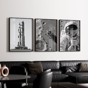 May include: A set of three black and white framed wall art prints. The first print shows a Saturn V rocket on a launch pad. The second print displays a lunar module on the moon surface. The third print features an astronaut in a space suit.