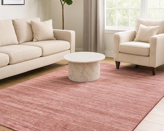Puede incluir: Una alfombra grande, rectangular, de color rosa polvoriento en un salón. La alfombra está colocada sobre un suelo de madera, con un sofá beige, un sillón y una mesa de centro con tapa de mármol. Una impresión enmarcada de helecho cuelga en la pared.