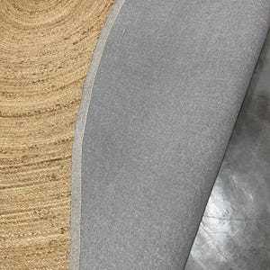 K&ouml;nnte beinhalten: Nahaufnahme eines Naturfaserteppichs mit Spiralmuster. Die Oberseite des Teppichs ist hellbraun, die Unterseite ist ein grauer Stoff. Der Rand des Teppichs ist sichtbar und zeigt den Kontrast zwischen den beiden Materialien.