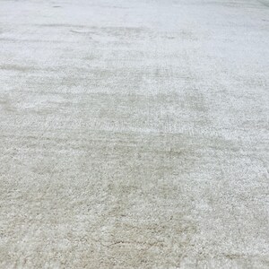 May include: A large area rug featuring a solid, light gray color with a soft, textured pile surface. The rug displays a consistent, dense weave throughout, creating a uniform appearance across the entire visible expanse of the floor covering.