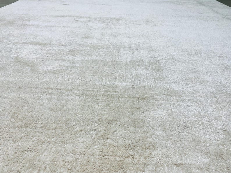 May include: A large area rug featuring a solid, light gray color with a soft, textured pile surface. The rug displays a consistent, dense weave throughout, creating a uniform appearance across the entire visible expanse of the floor covering.