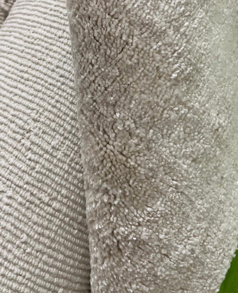 May include: Close-up of two sections of a light beige rug. One section has a ribbed pattern, while the other has a plush, textured surface. The rug appears soft and inviting, suitable for home decor.