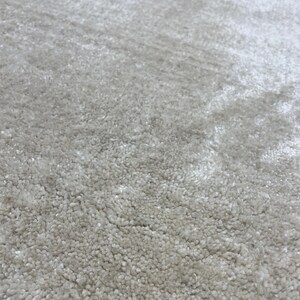 May include: Close-up of a light gray rug with a textured, plush surface. The rug's fibers create a soft, inviting appearance. The neutral color and dense pile suggest comfort and warmth, suitable for home decor.