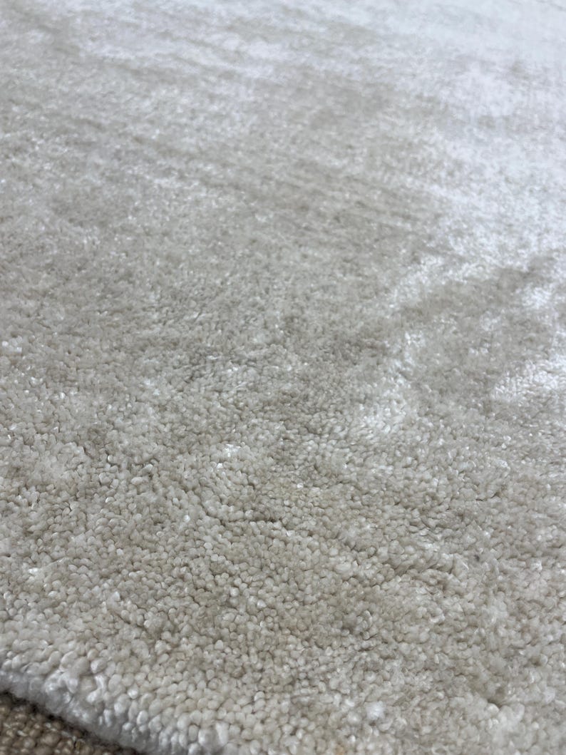 May include: Close-up of a light gray rug with a textured, plush surface. The rug's fibers create a soft, inviting appearance. The neutral color and dense pile suggest comfort and warmth, suitable for home decor.