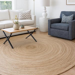 K&ouml;nnte beinhalten: Ein runder Jute-Teppich in Naturt&ouml;nen mit einem Spiralmuster steht im Vordergrund. Der Teppich liegt auf einem Holzboden in einem Wohnzimmer. Ein wei&szlig;es Sofa, ein Sessel und ein Couchtisch sind ebenfalls zu sehen.