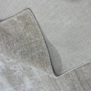 May include: Close-up of a light beige rug with a textured surface. The rug is folded over, revealing the underside and the edge of the rug. The rug appears to be made of a soft material.