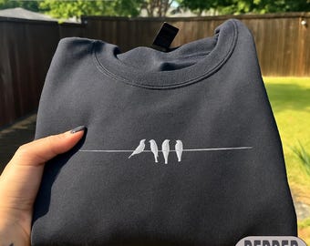 May include: A dark gray sweatshirt with a crew neck, featuring an embroidered design of three birds perched on a thin white line. The word "EMBROIDERY" is at the top, and "PEPPER" is at the bottom.
