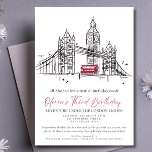Puede incluir: Tarjeta de invitación blanca con una ilustración en negro y rojo del Tower Bridge, un autobús de dos pisos rojo y el Big Ben. El texto dice "Olivia's Third Birthday" y los detalles del evento.