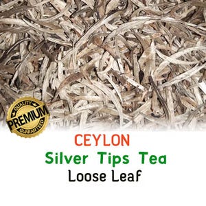 May include: A collection of dried, needle-like tea leaves in shades of silver, grey, and brown. A gold circular badge reads PREMIUM QUALITY GUARANTEED. Below the leaves, the text reads CEYLON Silver Tips Tea Loose Leaf in orange and green.