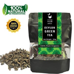Può includere: Un sacchetto nero di tè verde di Ceylon con un'etichetta verde e bianca. L'etichetta recita "Ceylon Green Tea" e "100% Pure Organic". Un mucchio di foglie di tè verde sfuse è accanto al sacchetto. Il sacchetto ha anche il testo "100% Natural" e "Premium Quality".