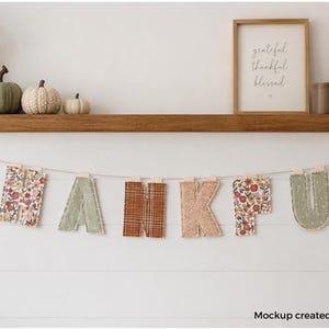 May include: A fabric banner spelling the word THANKFUL, featuring letters in various patterns including floral, plaid, and solid colours in shades of orange, green, and beige, suspended on a thin string against a white horizontal panelled wall.