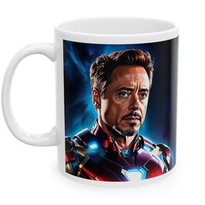 May include: White ceramic mug featuring a portrait of a man in a red and blue armored suit, with a blue and black background. The mug has a white handle and is likely a fan item.