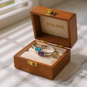 May include: A silver bracelet with a blue and purple rectangular gemstone design, displayed inside an open wooden jewelry box. The box is brown with a gold clasp and the text "MPDLMDL" inside.