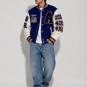 Può includere: Una giacca varsity blu e crema con una grande lettera A sul petto, il nome Adrian, una grafica circolare e il testo 283, 400, 4X1 sulla manica. La giacca presenta polsini a righe, una t-shirt bianca, jeans azzurri e scarpe da ginnastica bianche.