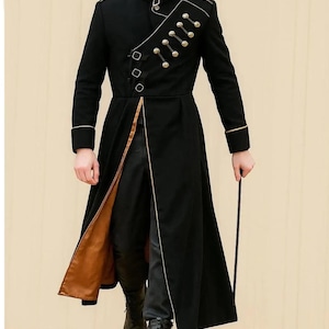 May include: Black military-style coat with gold trim and buttons. The long coat features a high collar, decorative buttons, and a split front revealing a brown lining. The coat is worn with black pants and boots, and a black cane.