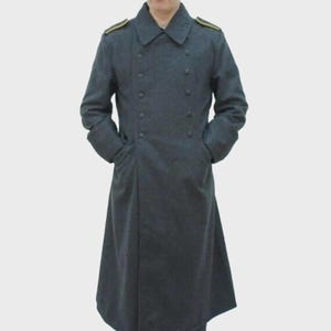 May include: A dark grey, double-breasted overcoat with a long, flowing design. The coat features a notched collar, button closures, and gold shoulder epaulettes. The person is wearing the coat with their hands in the pockets.