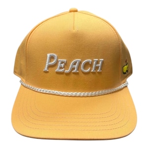 Può includere: Un cappellino da baseball color pesca con la scritta "PEACH" ricamata in bianco sul davanti. Un dettaglio in corda bianca rifinisce la visiera e un piccolo logo verde e giallo è sul lato. Il cappellino ha una visiera curva e una corona strutturata.
