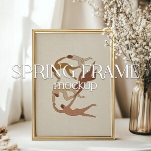 Può includere: Una cornice rettangolare dorata con il testo bianco "SPRING FRAME mockup". L'opera d'arte all'interno presenta figure stilizzate nei toni del marrone e beige. Un vaso di fiori bianchi è a destra.