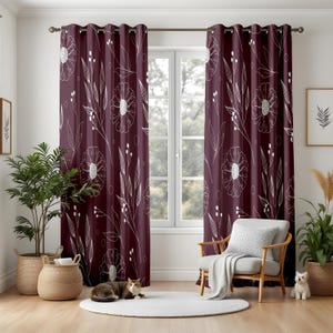 May include: Burgundy floral curtains with white outlines of flowers and leaves. The curtains hang in front of a window, with a white chair and a round white rug in front of the window. A cat is lying on the rug.