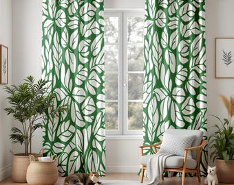 May include: Green and white leaf-patterned curtains hanging in front of a window. The curtains have a repeating design of large, stylized leaves. The room also features a chair, a round rug, and potted plants in woven baskets.