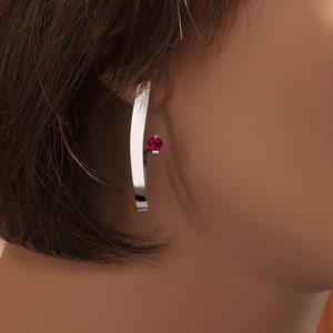 May include: Silver earring with a curved bar and a small red gemstone.