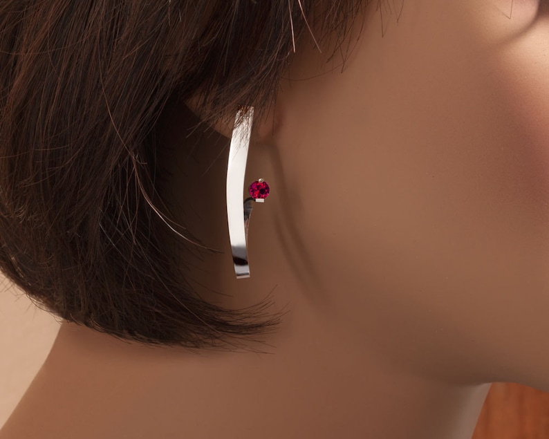 May include: Silver earring with a curved bar and a small red gemstone.