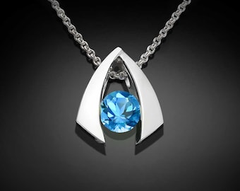 Puede incluir: Un collar de plata con un colgante que presenta una piedra preciosa azul engastada en un marco de plata. El colgante tiene la forma de una V invertida.