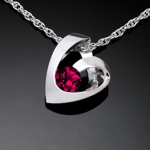 May include: A silver pendant necklace with a red gemstone set in a modern, abstract design.