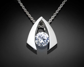 Puede incluir: Un collar de plata con un colgante en forma de triángulo invertido, adornado con una gran piedra preciosa redonda y transparente engastada en un marco de plata.